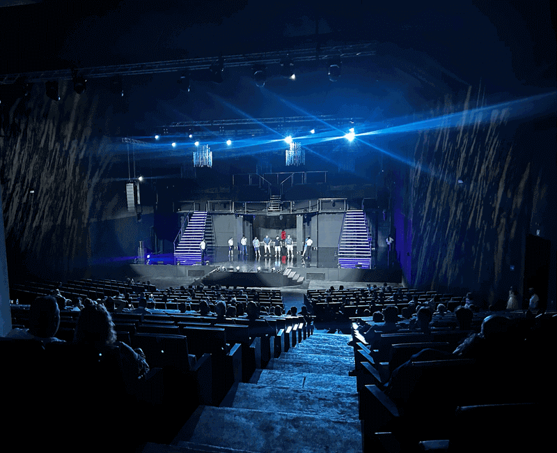 Guests sitting in a modern, vibrant resort theater watching a colorful pre-show performance on stage before the main event.