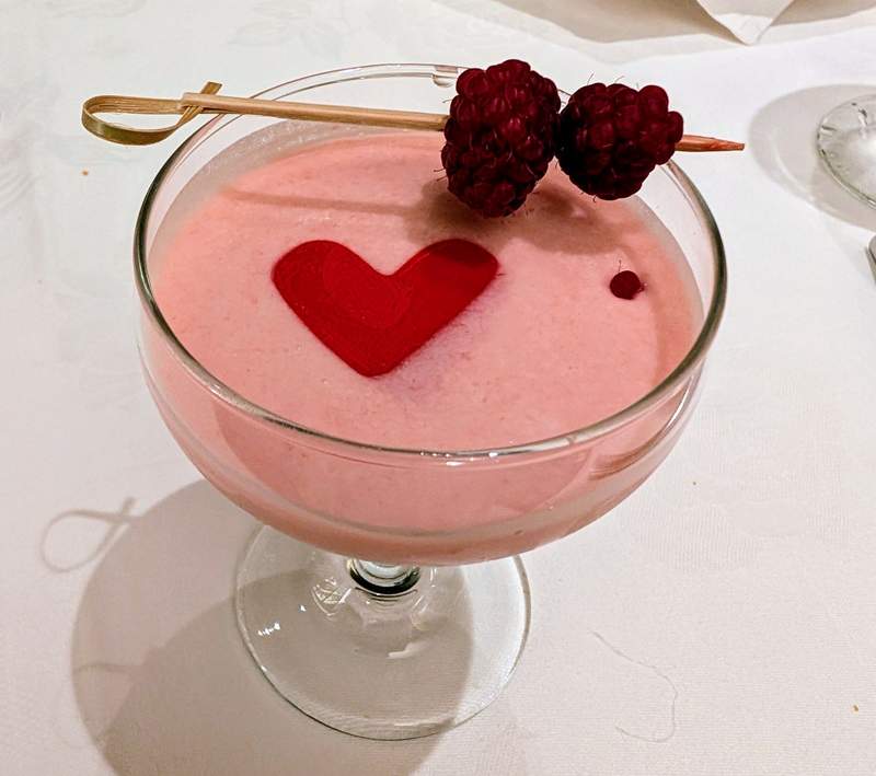 A pink cocktail with a red heart and raspberries