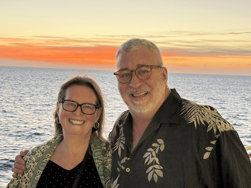 A happy couple smiling together against a beautiful golden sunset at sea on a cruise ship.