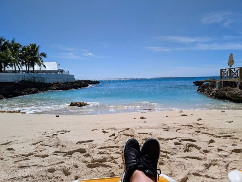 A pair of shoes left on a serene sand beach next to a secluded tropical ocean cove.