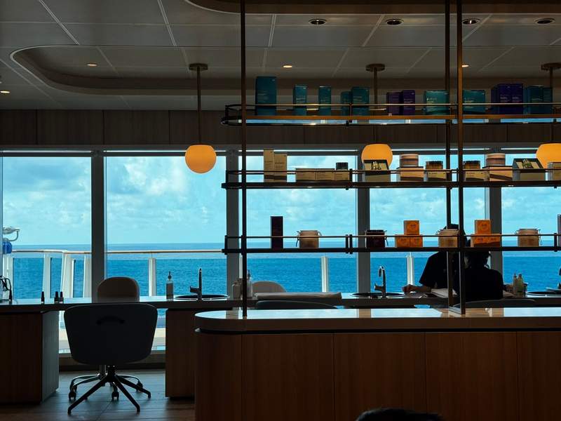 View from across the spa room during a pedicure, looking out at floor-to-ceiling windows and the sea.