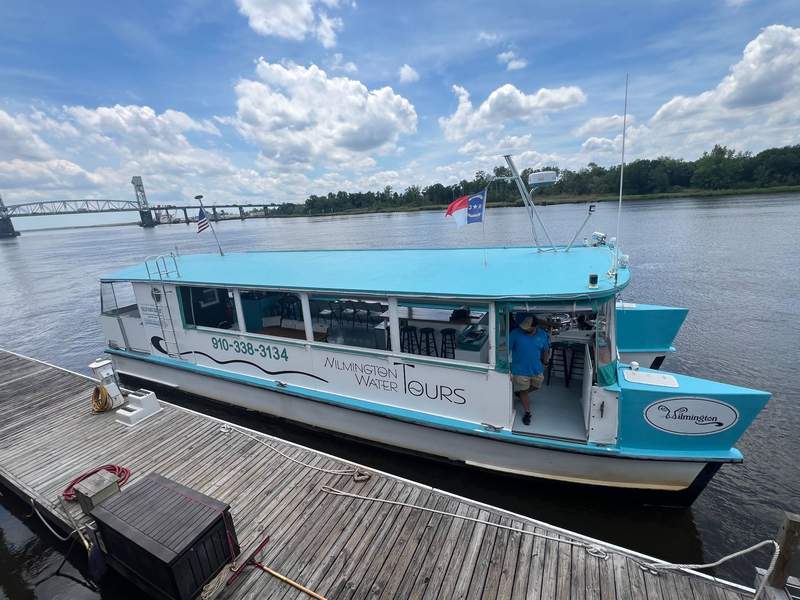 Blue boat docked in the Cape Fear River with bridge in the background.