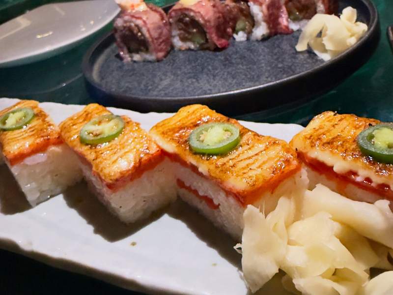 Close up of rectangular shaped salmon oshi at Miku with layered rice, special sauce, topped with salmon and a jalapeno slice.