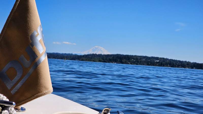 The bow of an electric boat cutting through blue water with the snow-capped peak of Mount Rainier on the horizon.