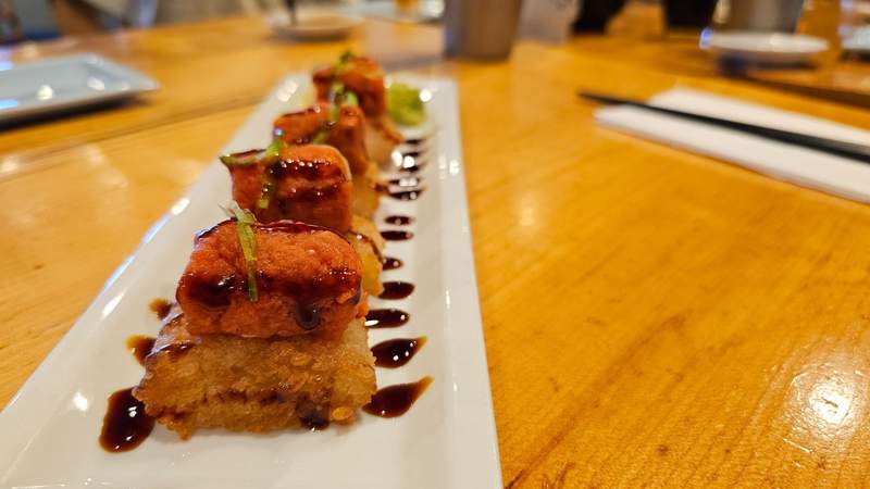 A close-up shot of crispy rice blocks topped with spicy tuna tartare and green jalapeno slices on a plate.