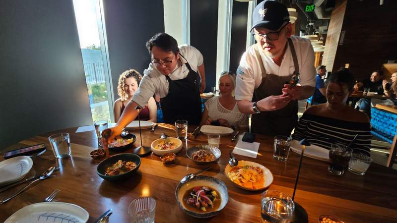 Wait staff at restaurant deliver several dishes to a table with ceviche