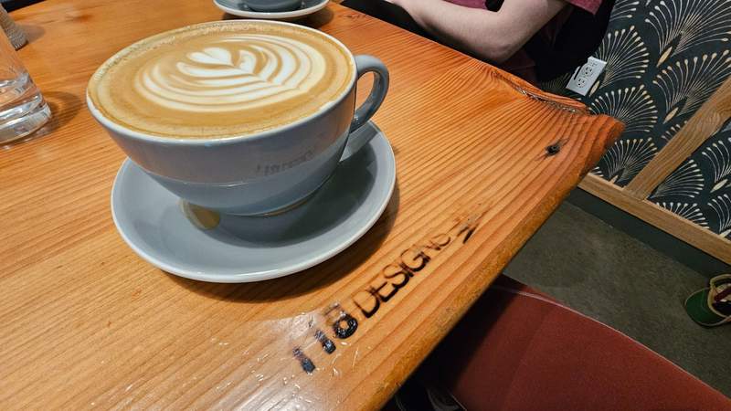 A cup of hot latte coffee sitting on a cafe table featuring intricate, elaborate leaf art poured into the foam.