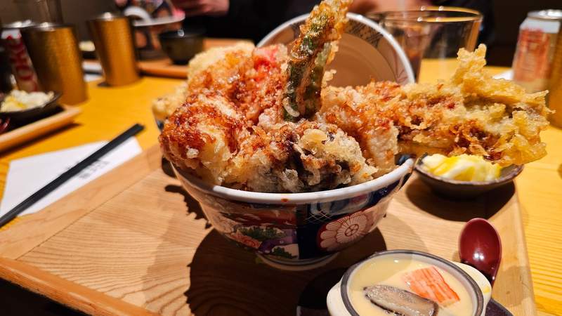 A large Japanese tendon bowl filled with assorted golden, crispy tempura prawns and vegetables.