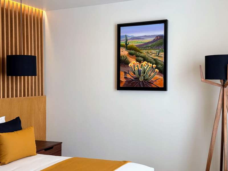 Contemporary hotel room with neutral tone bedding and framed Baja desert landscape art.