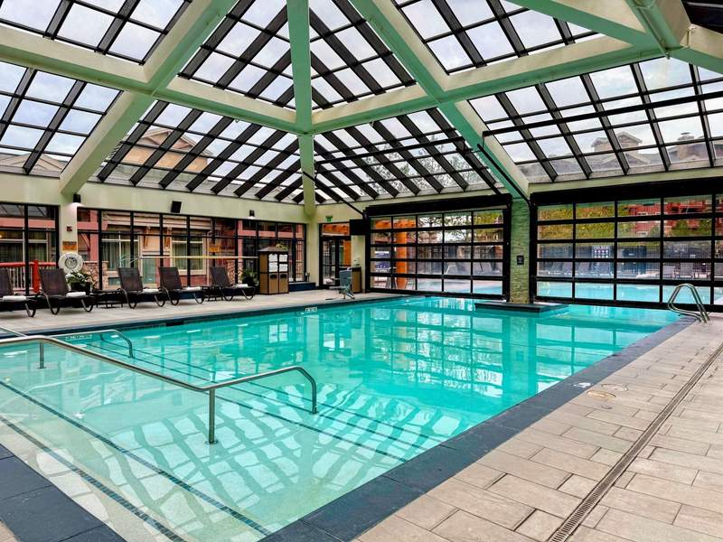 Indoor resort pool with glass ceiling and lounge chairs