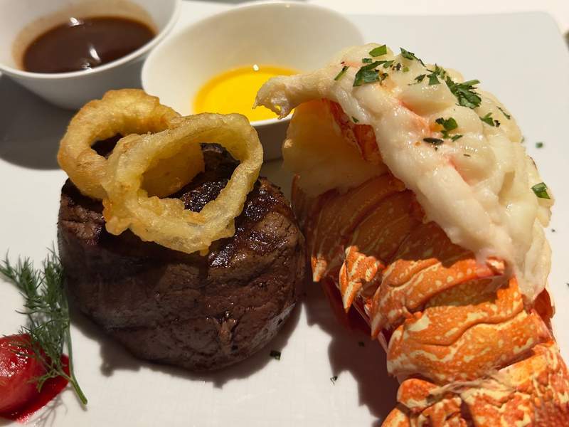 Filet mignon topped with a crispy onion ring, paired with broiled lobster tail, drawn butter, and peppercorn sauce on Holland America's Koningsdam.