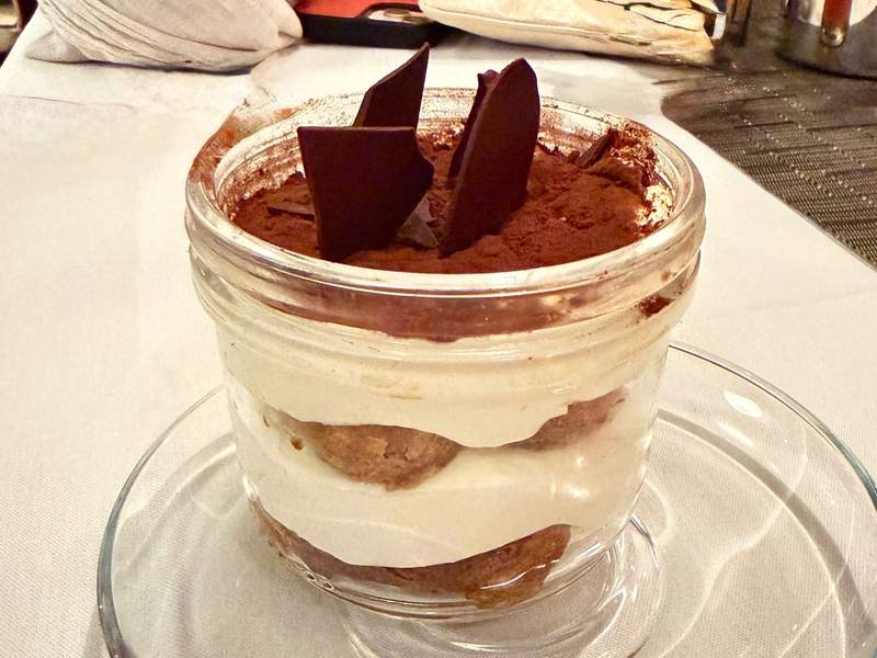 Layered tiramisu in a glass jar topped with cocoa powder and dark chocolate shards, served at Canaletto on Koningsdam.