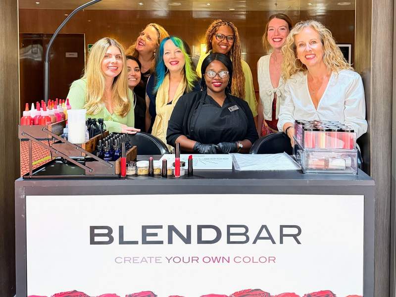 A group of smiling women posing with new lipstick behind Blendbar.