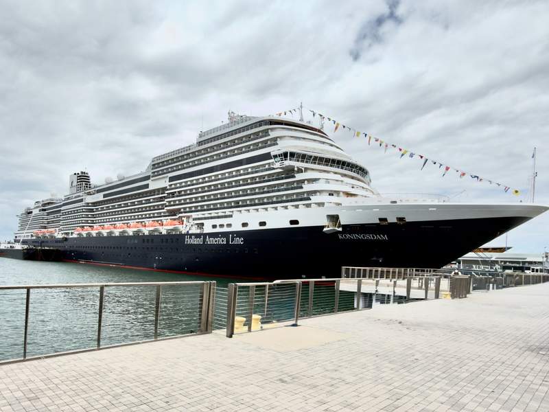 Side view of the large luxury cruise ship, Holland America's Koningsdam, docked at a concrete pier under a cloudy sky in San Diego.