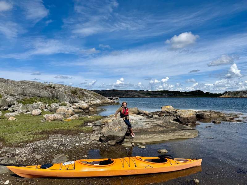 Woman wearing a red safety vest in front of an orange double kayak, surrounded by water and rocks in Gothenburg’s Southern Archipelago.