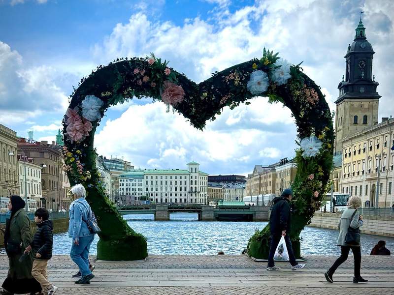 Large flower-covered heart framed by Gothenburg city views as people walk past.