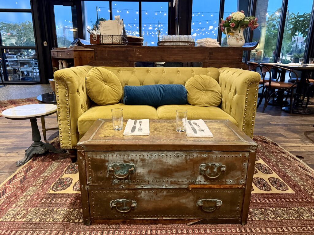 Olive green loveseat with dinner plates on an antique trunk at Oak and Ola, an Armature Works' friend trip restaurant in Tampa