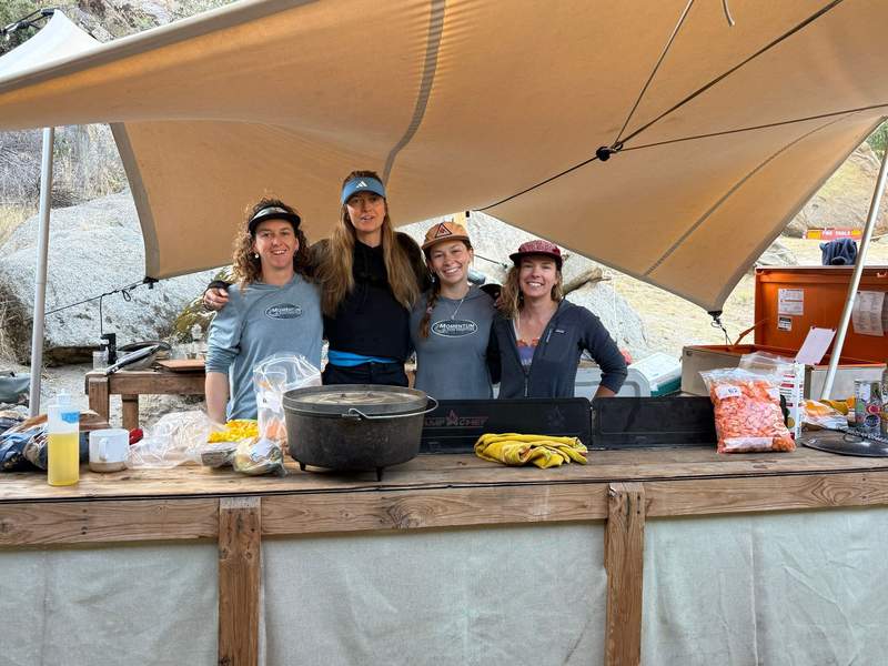 Guides and staff posing for a photo while prepping dinner under a canopy.