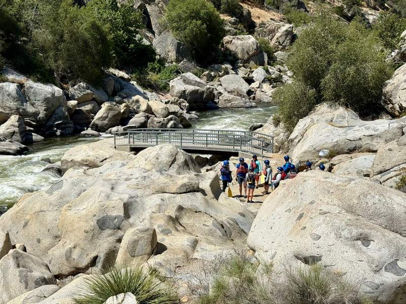 Group of rafters standing amidst some rocks and boulders with a ramp leading out to the Kern River.