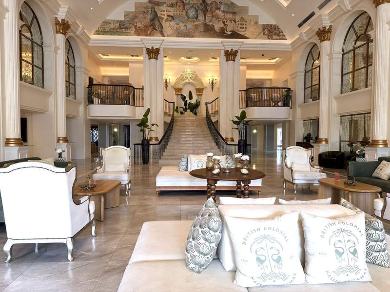 Interior view of the renovated historic lobby at the British Colonial Nassau resort in the Bahamas showcasing plush white seating columns and a grand staircase.