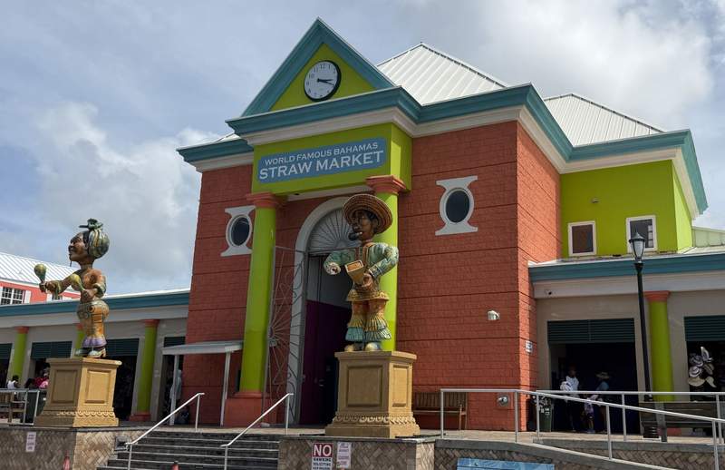 Exterior entrance of the World Famous Bahamas Straw Market in downtown Nassau featuring colorful Caribbean architecture and Junkanoo statues.