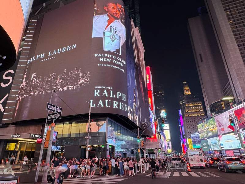 Huge billboard with Usher promoting Ralph Lauren, hundreds of people on the street at night with lighted billboards and cars along the street.