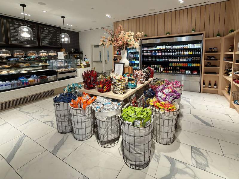 A market inside the Hilton Times Square with several bins filled with a variety of potato chips, refrigerated shelves with drinks, pastries and a sandwich counter.