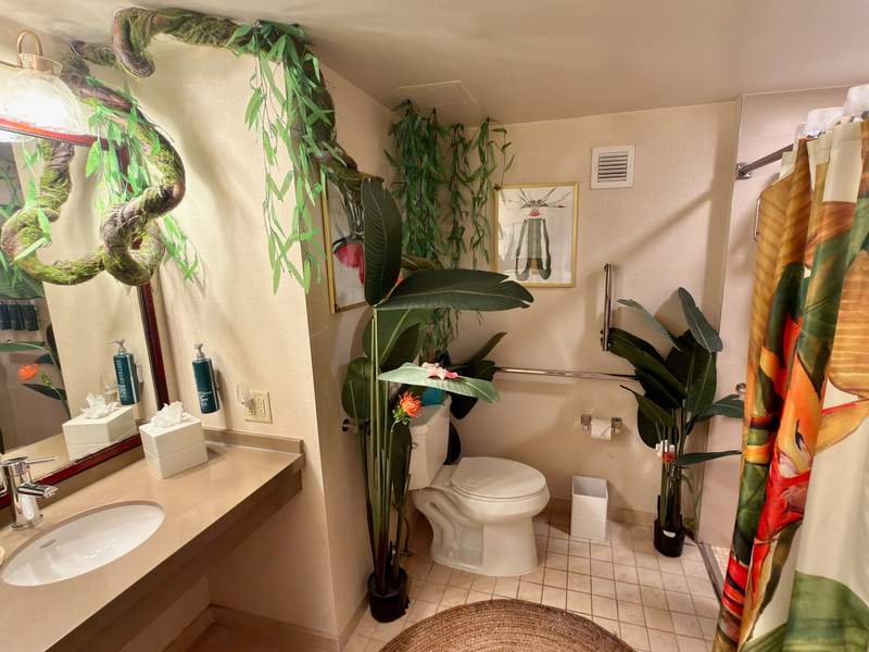 Lion King themed room at the Hilton Times Square with huge green tropical plants and a winding vine framing the bathroom mirror and a jungle themed shower curtain.