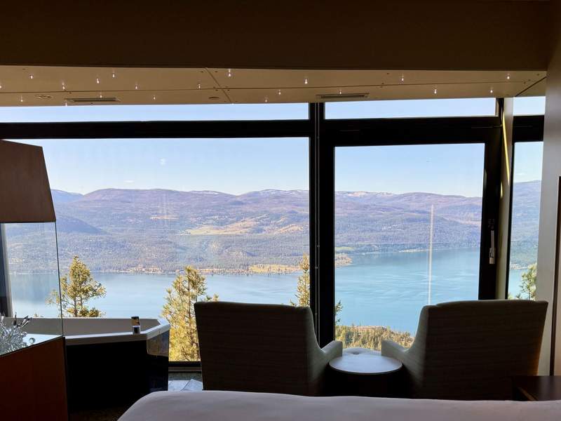 Hotel room with floor-to-ceiling windows with a view of a lake and mountains.