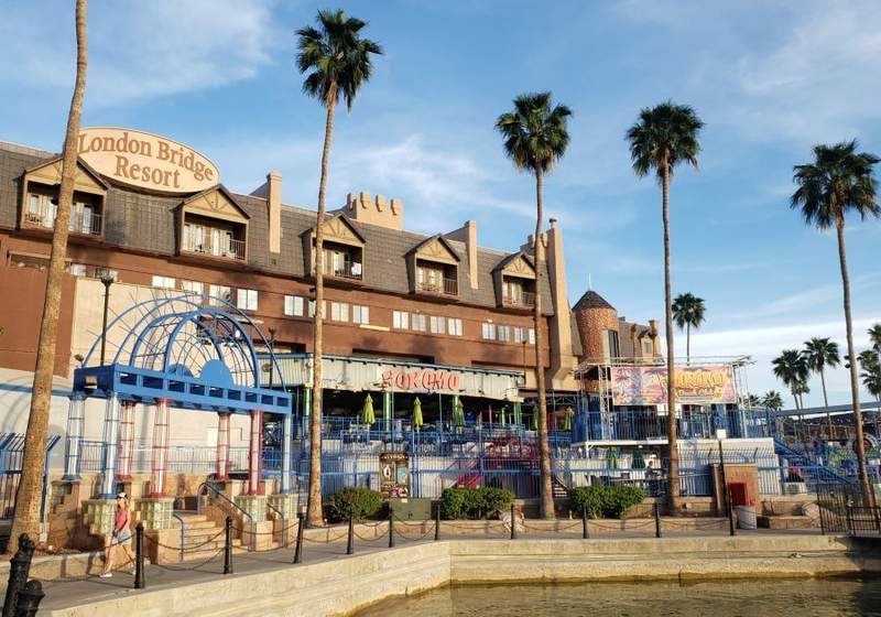 Panoramic waterfront view of the London Bridge Resort in Lake Havasu City, featuring swimming pools, waterslides, and palm trees under a blue sky.