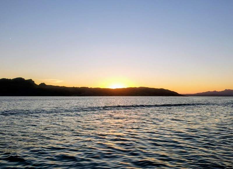scenic golden sunset over the mountain horizon, reflecting bright orange and pink light across the calm waters of Lake Havasu.