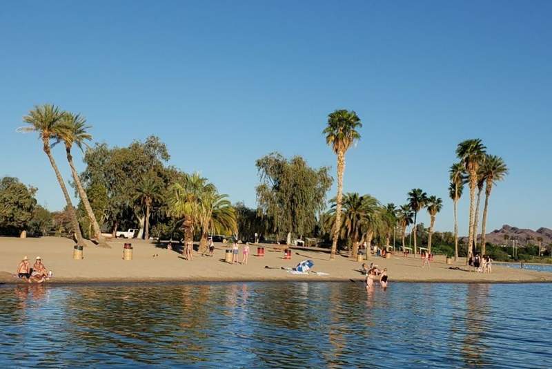 A calm sandy beach along the river shore in Lake Havasu, featuring distant mountain views and clear blue skies.