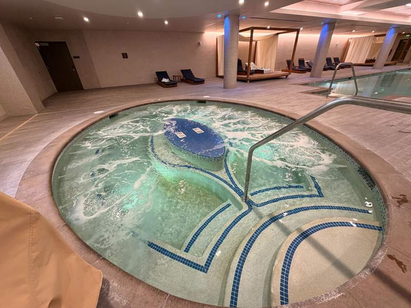Bubbling round inground hot tub with concrete steps edged with blue tile.