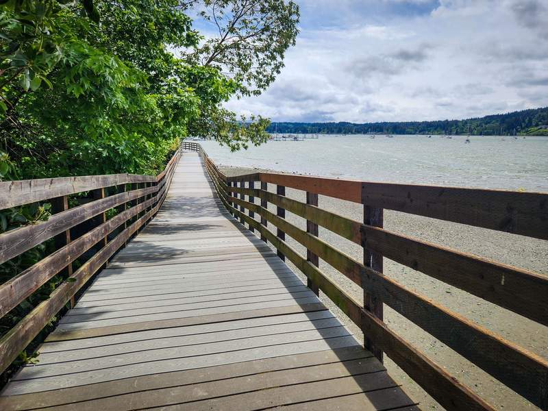 A wooden boardwalk with high side rails snakes along the shore of Liberty Bay