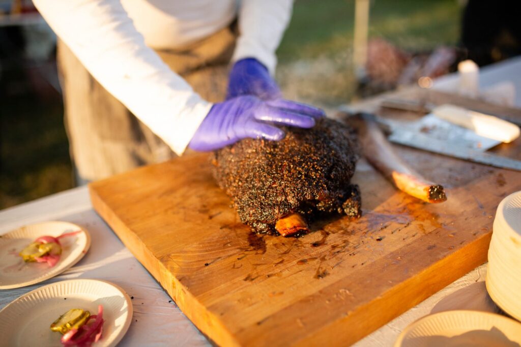 Carving meat at the Townsend Grain & Grits Festival. Photo credit Tennessee Tourism A person with purple gloves carving meat at the Townsend Grain & Grits Festival.