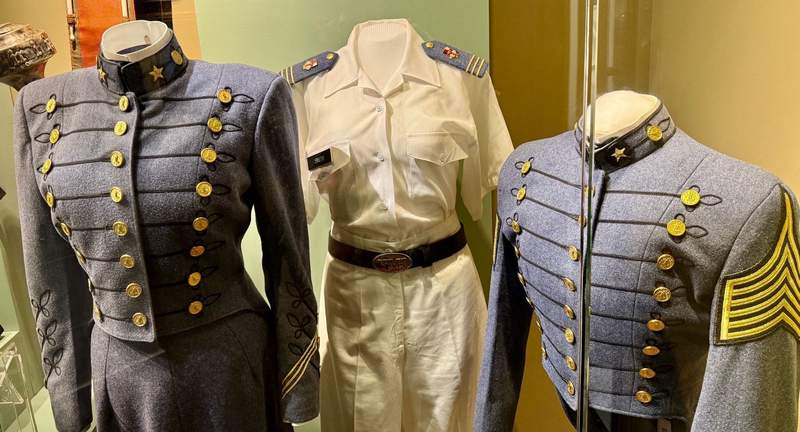 Tthree military uniforms in a glass display case.