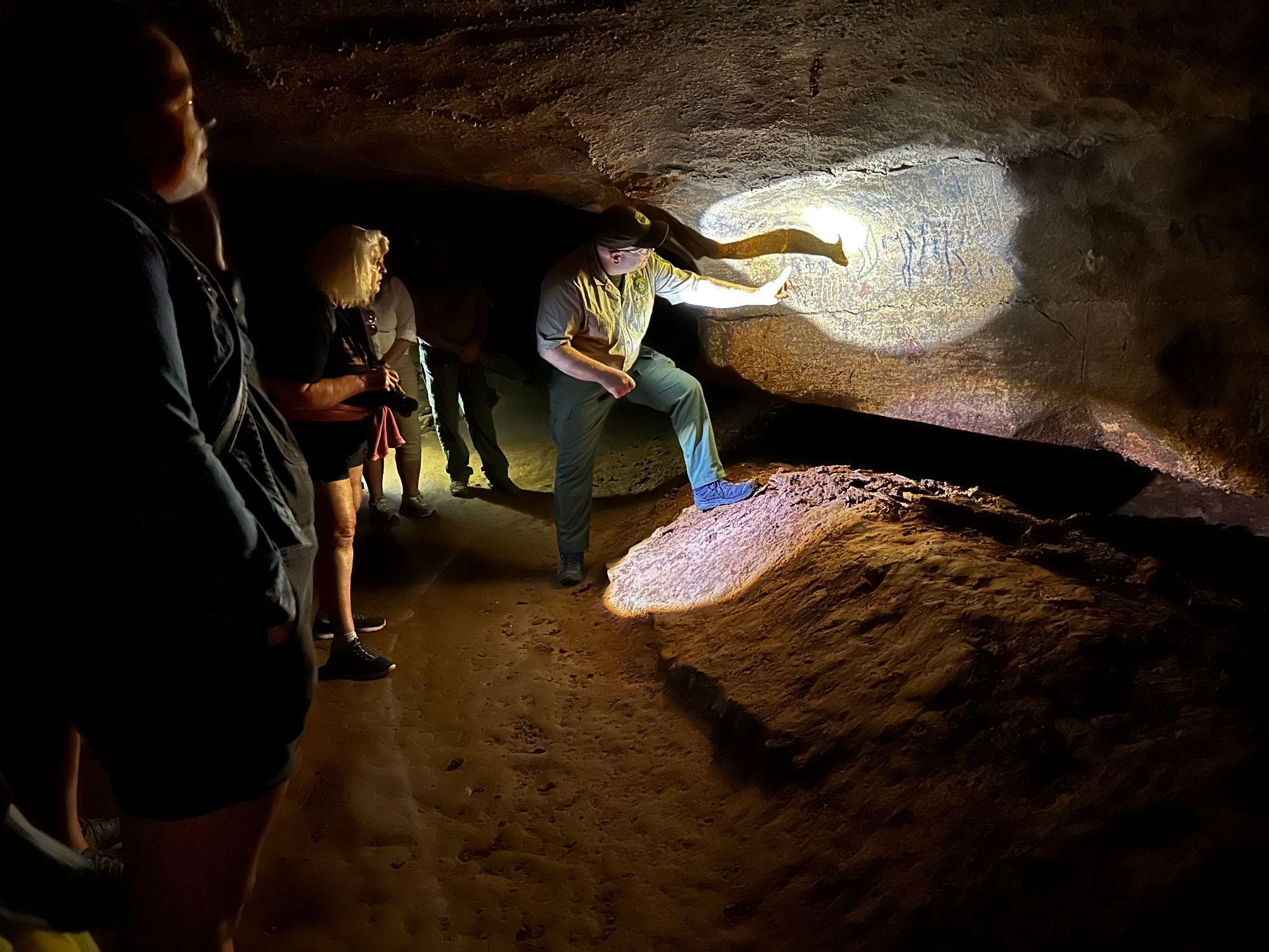 A light on the wall of a cave.  A man is pointing at something. 
