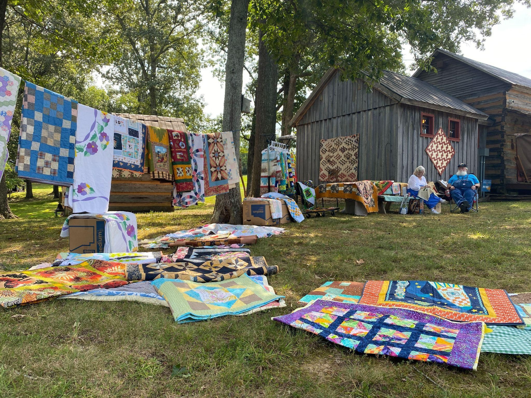 Quilts hanging on a line and laying on the ground. 