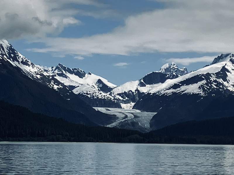 Aerial view from a floatplane window showing dark blue ice crevasses and swirling patterns across a massive Alaskan glacier.