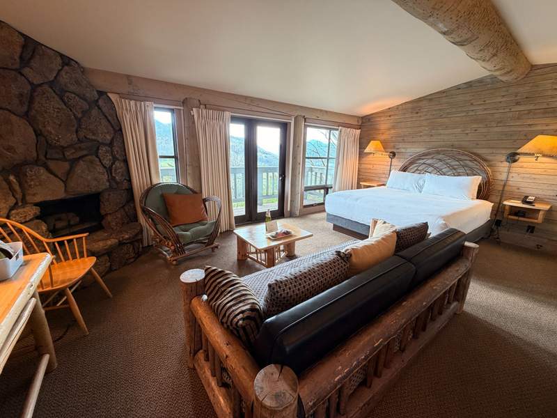 A western themed room with rustic bent-willow furniture with a king bed, sofa, chair and a stone fireplace with mountain views.