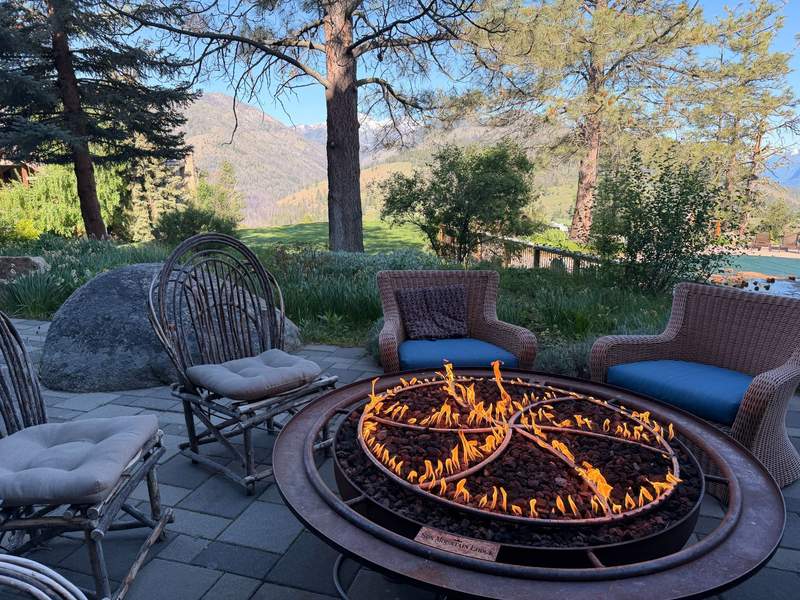 Wagon-wheeled shaped firepit with flames surrounded by plush seating. Patio overlooks the North Cascade Mountains.