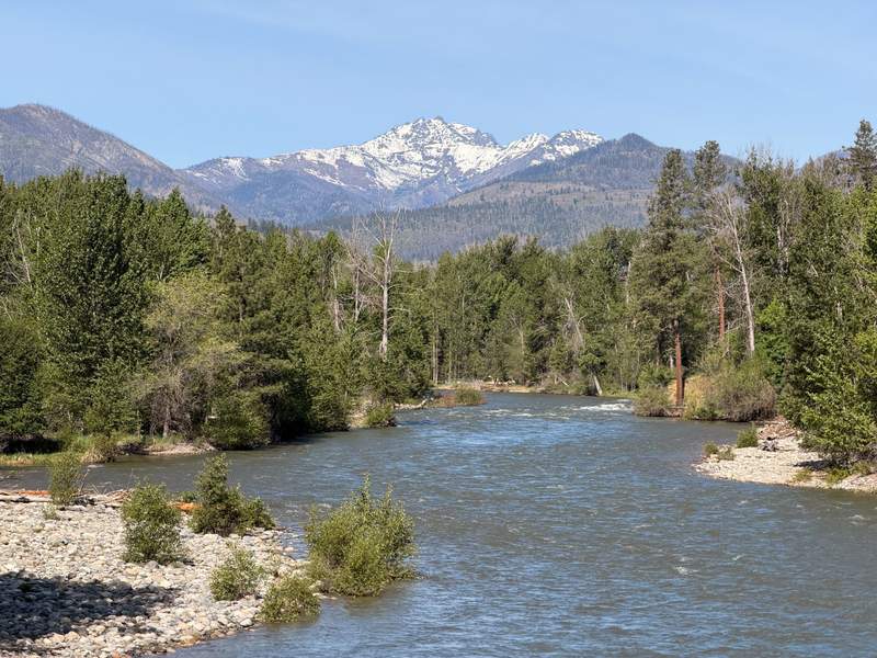 The Methow River flows between wooded, rocky banks, with Mt. Gardner and the North Cascade Mountains visible in the distance.