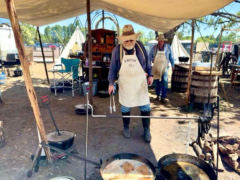 Chuckwagon Cookoff crew preparing food over an open fire beside a traditional canvas-covered wagon at Cheyenne Frontier Days.