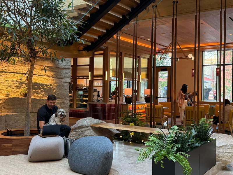 The Compton Hotel in Bentonville, Arkansas, has a spacious lobby and is pet-friendly, showing a dog on a guest’s lap.