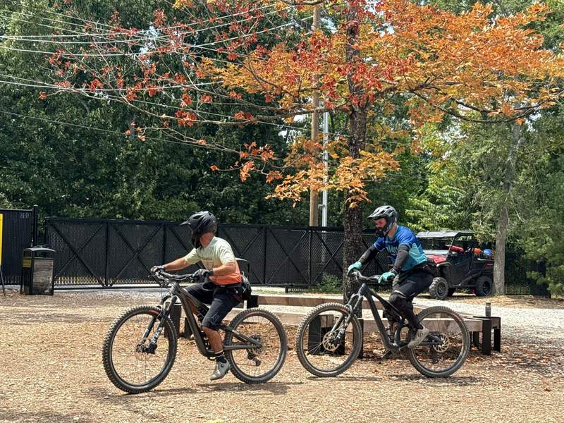Two mountain bikers ride past a fall foliage tree at Oz Trail Bike Park in Northwest Arkansas.