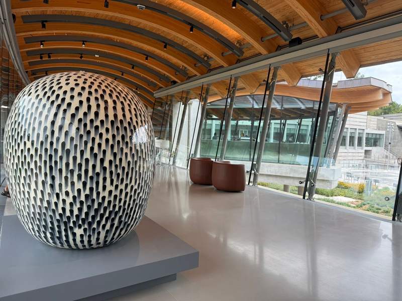 A large piece of artwork on display inside Crystal Bridges Museum of Art in Bentonville, Arkansas, overlooks glass windows.