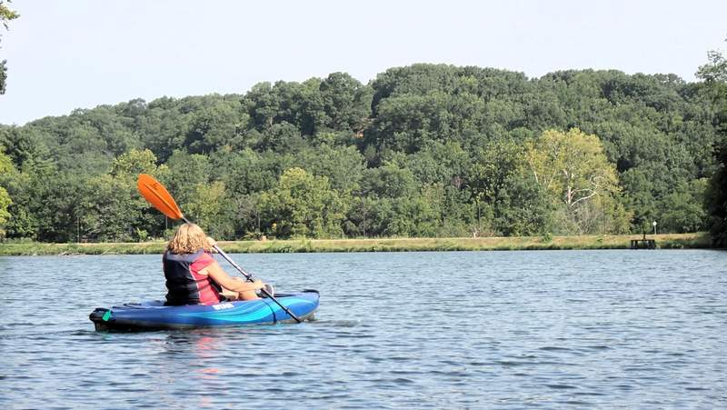 A woman kayaks on a lake surrounded by green trees in Northwest Arkansas.