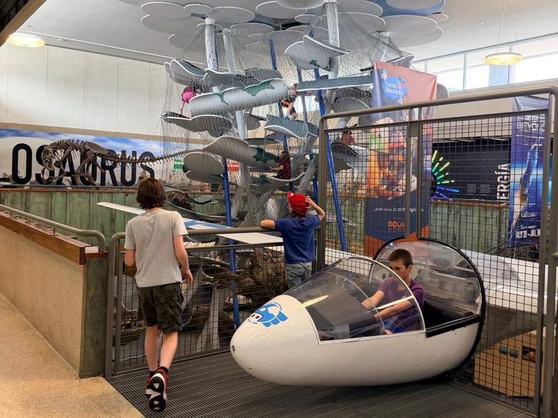 Three boys at The Discovery with the Cloud Climber and Allosaurus in the background. The Discovery is a participating venue in the Reno Artown Festival.