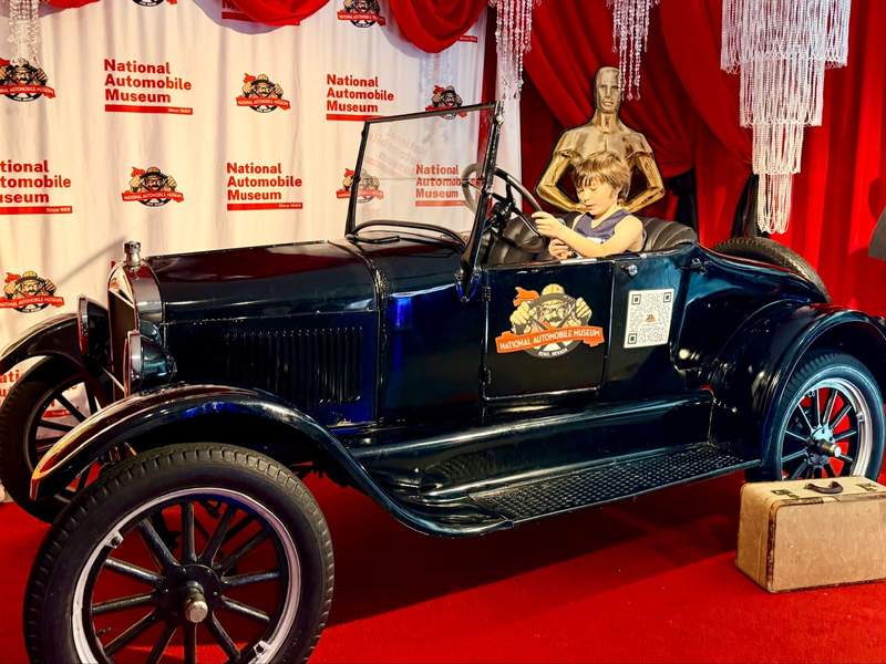 Boy sits in driver’s seat of antique car at the National Automobile Museum.