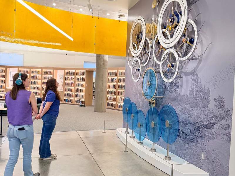 Two teen girls look at a clock art piece at the Nevada Art Museum. One girl is wearing noise-cancelling headphones.
